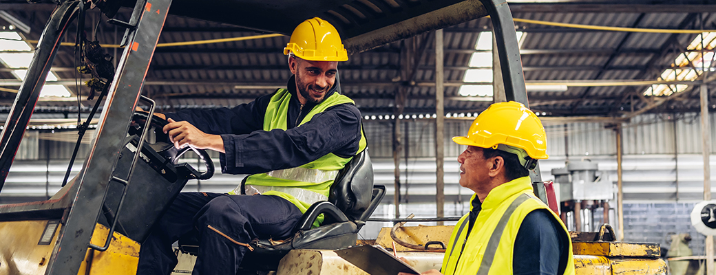 Image of a warehouse worker sitting in a forklift while speaking to another worker